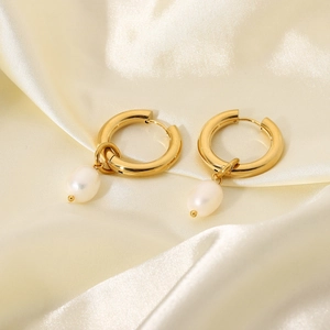 Detail of 18k gold plated hoop earrings with white drop pearls on beige silk fabric
