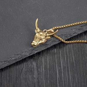 Macro detail of golden bull head pendant and rolo chain on textured dark stone