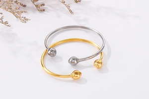 Detail of open cuff bracelets with spherical ends in polished gold and silver steel finish