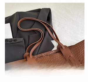Détail d'un sac cabas marron en cuir gaufré avec de longues anses sur un blazer