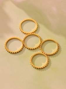 Detailed view of 5 stackable gold gear-shaped rings with gear texture on green background