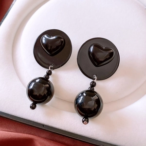 Detail of vintage black round earrings with embossed heart design in a white jewelry box