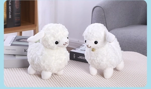 Close-up of two white plush alpaca toys with bells on a cozy woven mat indoors