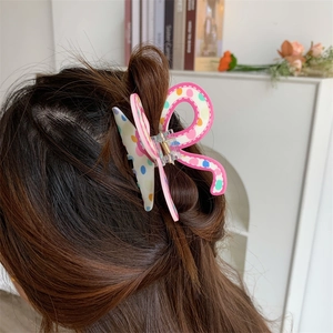 Detail of a wavy acrylic hair claw clip with colorful polka dots on long brown hair