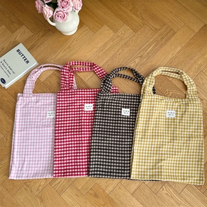 Flat lay of plaid canvas tote bags in four colors on a wooden floor with floral decor