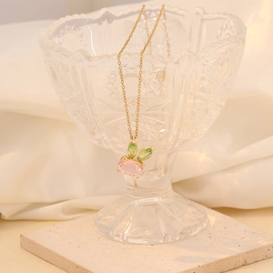 Golden bunny pendant necklace with pink and green stones in a glass on white fabric