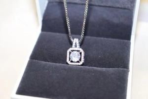 Macro detail of silver square zircon necklace pendant on dark grey velvet lining