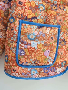 Close-up of quilted floral jacket featuring contrast blue trim and orange flower pattern