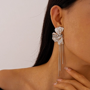 Dettaglio macro di orecchini a nappa argentati con design a petalo di fiore plissettato e frange