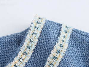 Detailaufnahme von blauem Tweed-Stoff mit beigen Fransen, blauen Pailletten und Goldkette