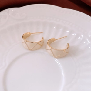 Detail of vintage 18k gold plated C-shape earrings with white enamel and grid texture
