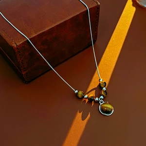 Artistic detail of round tiger eye stone pendant on silver chain over brown leather