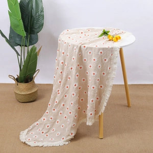 Close-up of muslin baby blanket with orange daisy patterns and white fringe edge detail