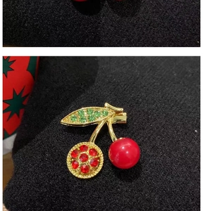 Macro shot of cherry brooch with red rhinestones and green crystal leaves on black fabric