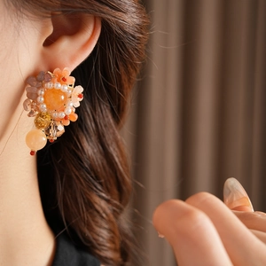 Gros plan d'une boucle d'oreille fleurie orange avec perles et cristaux sur un modèle
