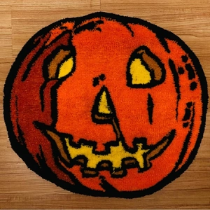 Round pumpkin face Halloween doormat with plush texture on dark wood floor