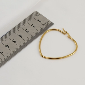 Detailed view of an 18K gold heart earring with ruler measuring size on white cloth