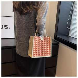 Detail of orange and white plaid woven tote bag with a white button closure and cotton handle