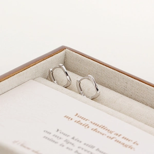 Macro detail of irregular wavy S925 silver hoop earrings on a minimalist jewelry display
