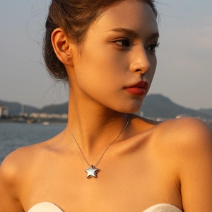 Elegant silver star pendant necklace worn by model against a scenic sunset beach background