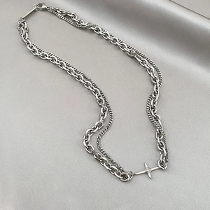 Macro detail of silver double-layer metal necklace with cross pendant on gray satin