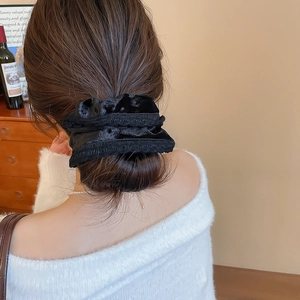 Detail of a black velvet scrunchie on a bun hairstyle with rich folds and texture