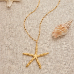 Collier en acier inoxydable plaqué or 18 carats avec pendentif étoile de mer sur lin beige