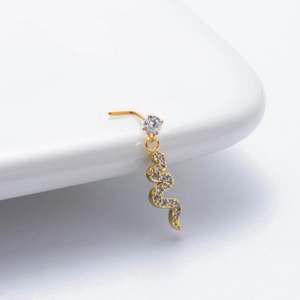 Macro shot of gold snake nose stud with sparkling zircon stones on a white ceramic plate