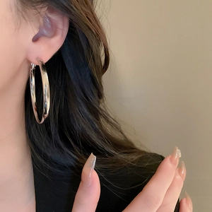 Macro shot of large polished silver hoop earrings worn on ear with reflective finish
