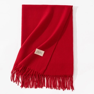 Detail of red celebratory scarf featuring soft fringe and woven brand label on surface