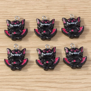 Close-up of small black bat charms with pink wing details and silver rings for DIY jewelry
