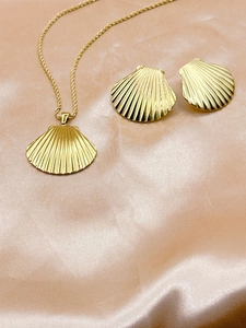 Detailed view of golden shell pendant necklace and earrings on pink silk fabric