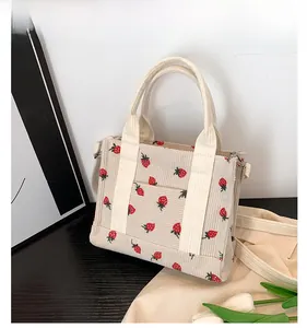 Detail of cream corduroy tote bag featuring red strawberry print and dual handles