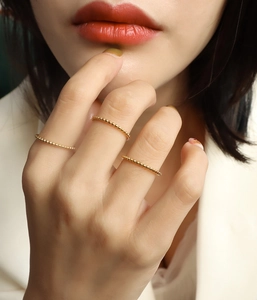 Close-up of thin 18k gold-plated beaded rings worn by a model in a layered style