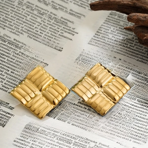 Close-up of golden square earrings with woven texture on vintage book pages