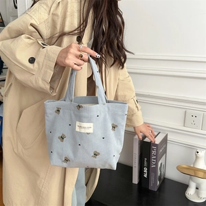 Close-up of light blue corduroy handbag with bear embroidery and soft texture detail