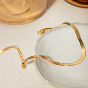 Detail of 18K gold stainless steel snake chain anklet on a white ceramic plate