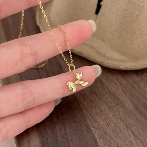 Detailed close-up of a golden ribbon bow pendant with fine textured metal surface on a thin chain