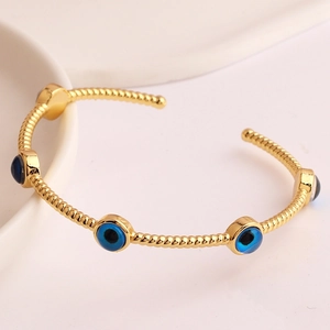 Detail of twisted gold-plated bangle with blue evil eye charms on white ceramic