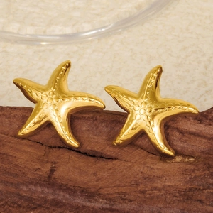 Macro detail of golden starfish earrings with textured finish on a rustic wooden base