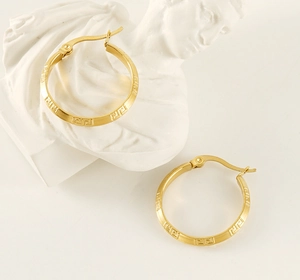 Macro detail of gold-plated hoop earrings featuring classic Greek fret pattern on white bust