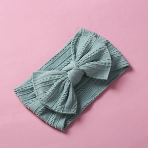 Detail view of mint green cable-knit baby headband with a large bow on pink background