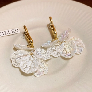 Macro detail of gold earrings with pearl-white textured flower petal tassels on ceramic