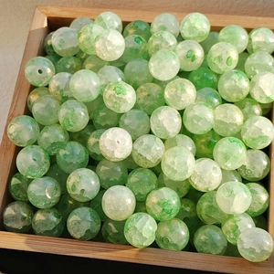 Macro shot of green and white cracked glass beads on a wooden tray for DIY jewelry