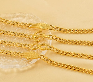 Détail de bracelets gourmette dorés avec breloques ancre, aile d'ange et main de fatma