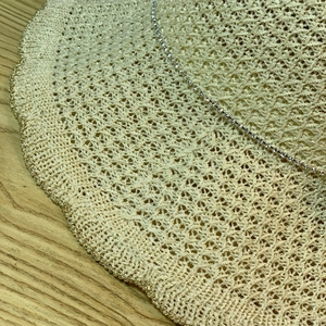 Macro shot of wavy gold-edged brim and rhinestone chain on beige straw sun hat