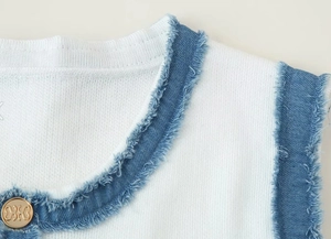 Close-up of white knit dress featuring blue denim raw-edge collar and gold button detail