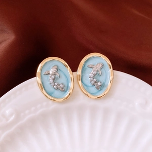 Detail of oval blue enamel earrings with silver fish motif and small pearls on white porcelain