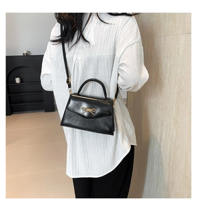 Détail du sac à bandoulière noir avec boucle en nœud doré et finition polie brillante