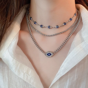 Macro detail of silver-tone layered necklaces featuring a crystal evil eye pendant